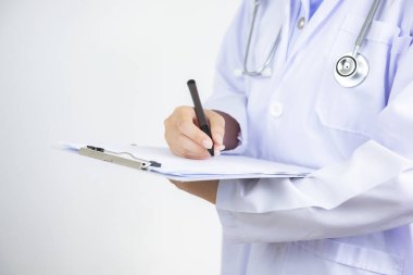 Hastane koridorunda dosyaları ve steteskopu olan doktor elinde pano ve reçeteli ilaç tutuyor.