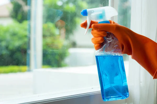 Hand in orange gloves cleaning window pane with spray Cleaning concept Prevent various virus infections