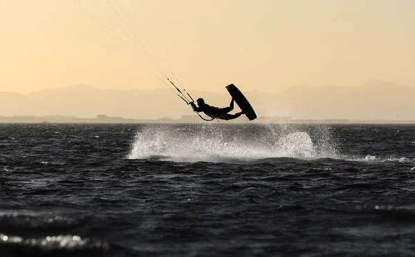 Kite boarding sportsman under sunset sun, freestyle kiteboarding
