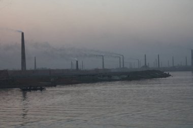 Buriganga Nehri kıyısındaki tuğla fabrikaları. Bu fabrikaların bacalarından çıkan kara duman çevreye ve ekosisteme ciddi bir tehdit oluşturuyor. Dhaka, Bangladeş