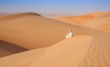 Arap adam bir kumul Arap Çölü'nde üzerinde oturan Kandoura ve 