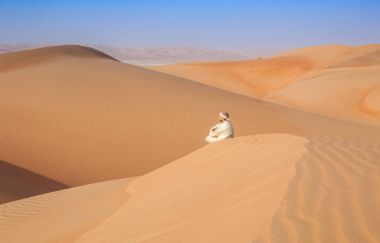 Geleneksel kıyafeti Arap Çölü'nde bir kumul üzerinde oturan omani adam