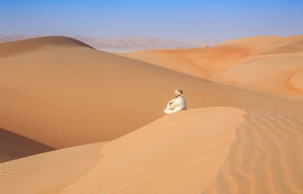 Omani man in traditional outfit sitting over a Dune in arabian Desert — Stock Photo, Image