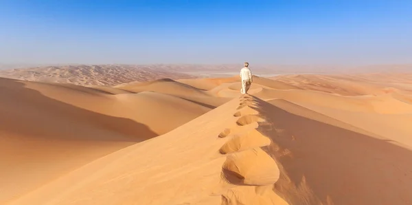 Arab man in local kandoura outfit walking over a Dune in arabian desert of abu dhabi — Stock Photo, Image