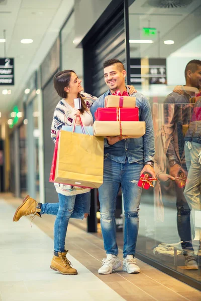 Paar met Kerst presenteert, geschenken en boodschappentassen in een winkelcentrum — Stockfoto