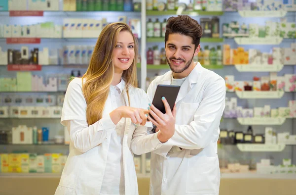 Farmacêuticos que usam comprimidos digitais enquanto verificam medicamentos em phar — Fotografia de Stock