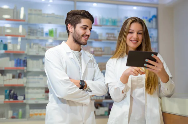Farmacêuticos que usam comprimidos digitais enquanto verificam medicamentos em phar — Fotografia de Stock
