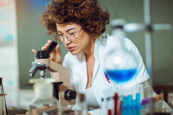 Mujer cientista en laboratorio. Joven científico mirando a través de un — Foto de Stock