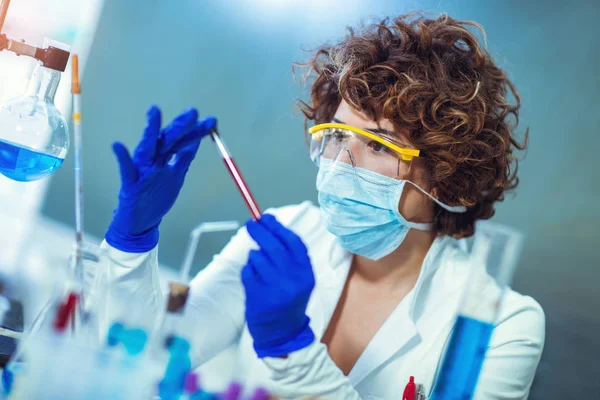 La mujer está sentada en la mesa en el laboratorio y sostiene el tubo de análisis de sangre — Foto de Stock