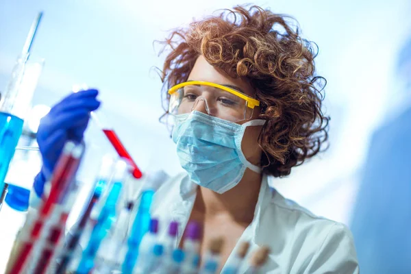 Woman is sitting at table in lab and holding blood test tube — Stock Photo, Image