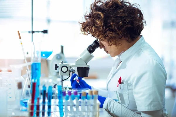 Woman scienist in laboratory. Young scientist looking through a — Stock Photo, Image