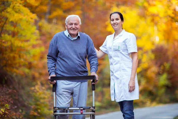 Sjuksköterska att hjälpa äldre senior man. Äldre man med en rullator med — Stockfoto