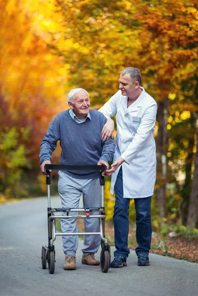 Manliga sjuksköterska bistå senior patienten med walker utomhus — Stockfoto