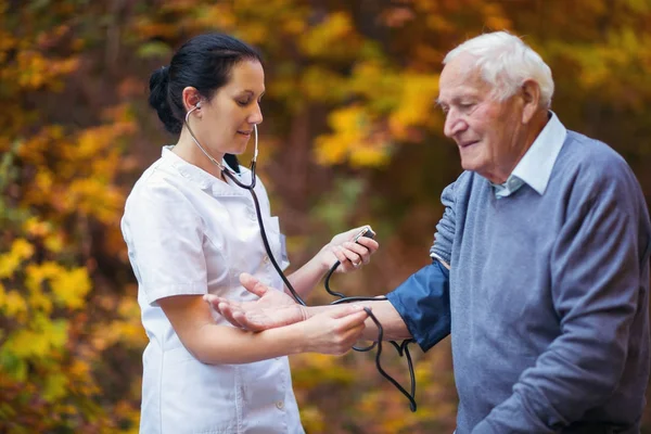 Медсестра измеряет давление у пожилых пациентов на открытом воздухе — стоковое фото