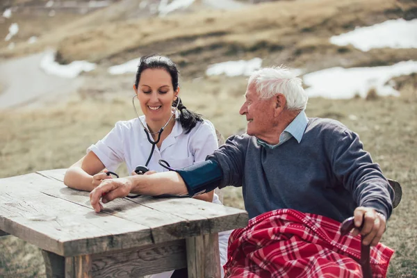 Sjuksköterska mäta gamla patientens blodtryck utomhus — Stockfoto