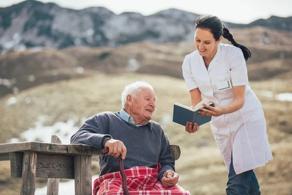 Leende Sjuksköterska Läsa Bok Till Senior Lycklig Utomhus — Stockfoto