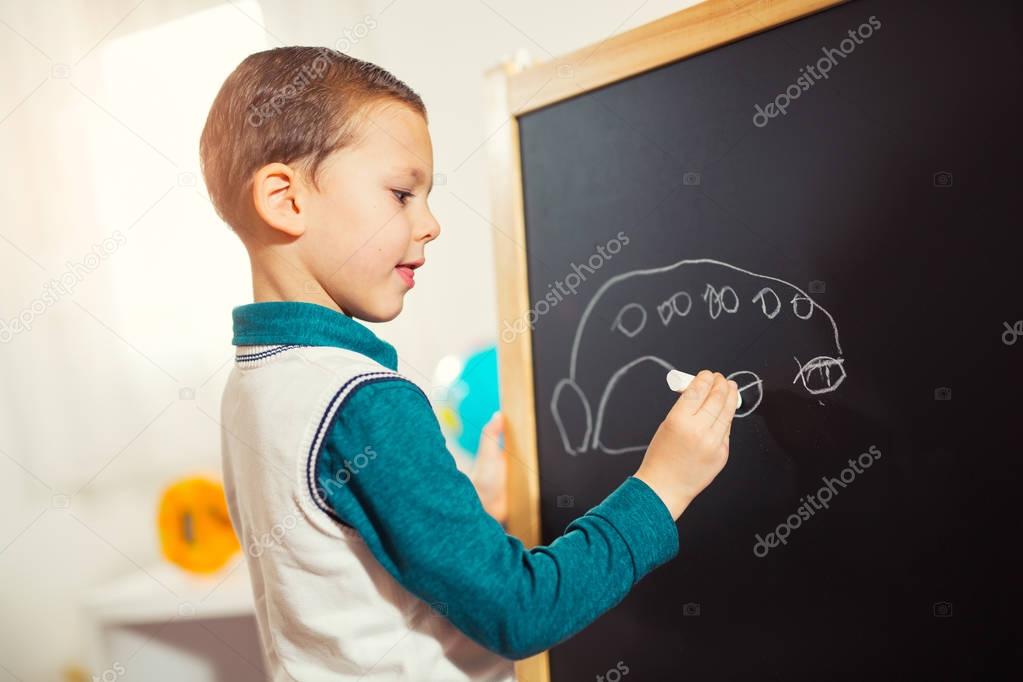 childish scribbles, little boy drawing with chalk on blackboard