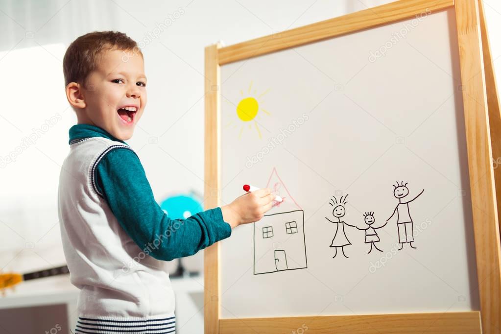 smiling cute little boy drawing on white board with felt pen. Early education concept
