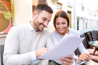 Genç mutlu çift konuşmak ve belgeleri kafede bakarak 