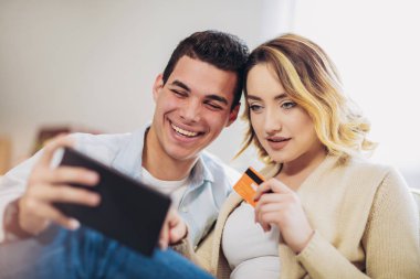 online alışveriş için dijital tablet ve kredi kartı kullanarak evde oturan genç mutlu çift 
