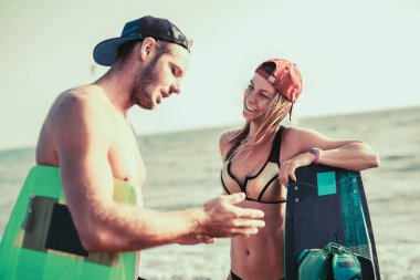 portrait of happy active couple of kitesurfers with boards at beach clipart