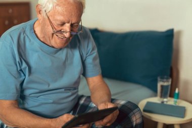 Dijital tablet evde kullanma yatağın üstüne oturan mutlu üst düzey adam 