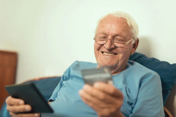 Šťastný Starší Muž Sedící Posteli Pomocí Digitálního Tabletu Kreditní Kartou — Stock fotografie
