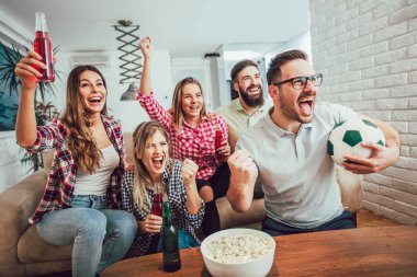 Mutlu arkadaşlar ya da futbol taraftarları televizyonda maç izleyip zaferi evde kutluyorlar. Dostluk, spor ve eğlence kavramı..