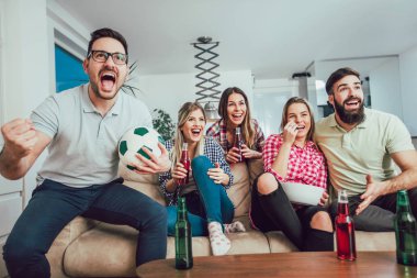 Mutlu arkadaşlar ya da futbol taraftarları televizyonda maç izleyip zaferi evde kutluyorlar. Dostluk, spor ve eğlence kavramı..