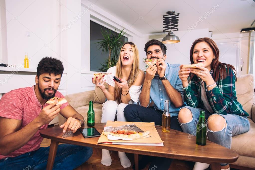 Friends and pizza. Four young cheerful people eating pizza at home.