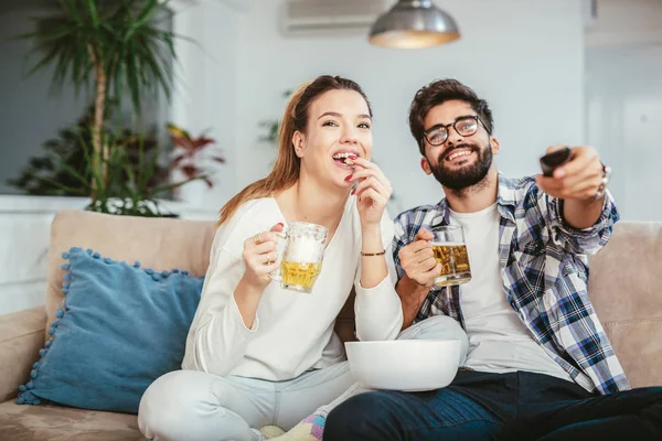 リビング ルームでテレビを見ながらポップコーンを食べて ビールを飲むカップル — ストック写真