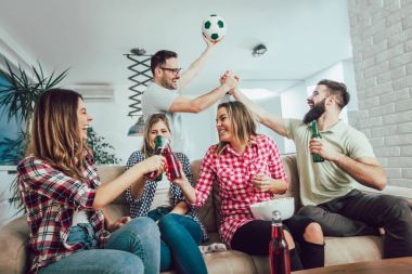 Mutlu arkadaşlar ya da futbol taraftarları televizyonda maç izleyip zaferi evde kutluyorlar. Dostluk, spor ve eğlence kavramı..