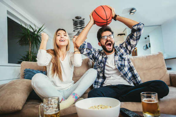 Couple is watching basketball game on the sofa at home.
