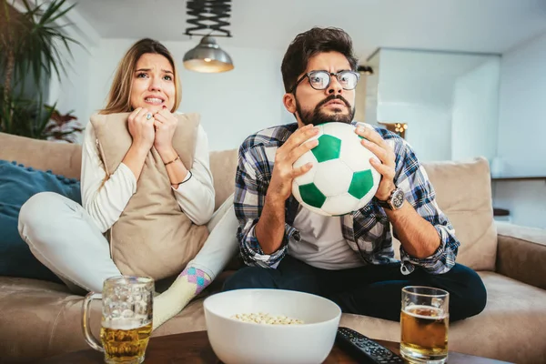 Couple is watching football on the sofa at home.