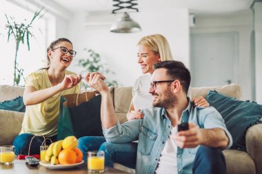 Sonra alışveriş torbalarıyla evde oturan genç kadınlar. Genç adam TV izlerken.