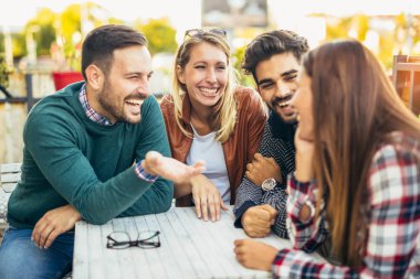 Bir grup arkadaş birlikte kahve içiyorlar. İki kadın ve iki erkek kafede gülüp eğleniyorlar.