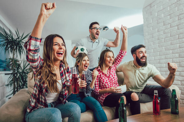 Happy friends or football fans watching soccer on tv and celebra