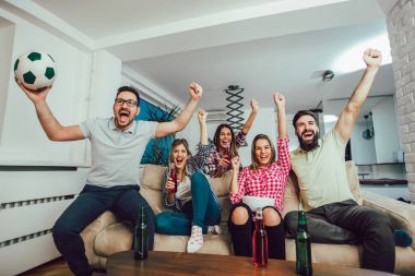 Mutlu arkadaşlar ya da futbol taraftarları televizyonda maç izleyip zaferi evde kutluyorlar. Dostluk, spor ve eğlence kavramı..