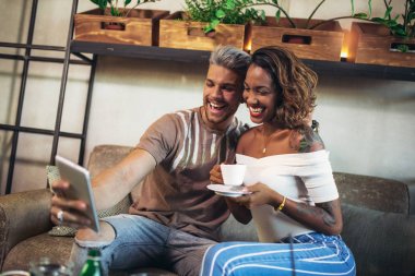 İki mutlu karışık yarış çift dijital tablet kullanarak kahve dükkanında eğleniyor