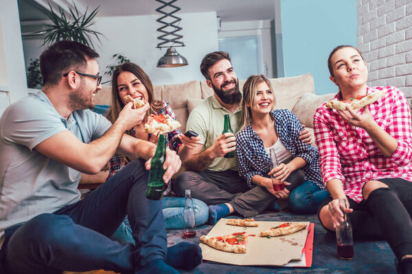 Group of young friends eating pizza at home party.