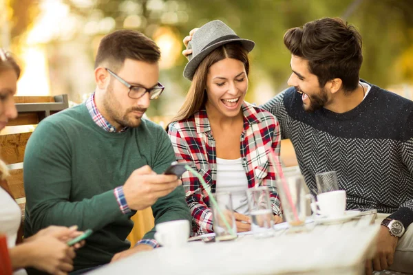 Group of four friends using smartphones, having fun and coffee together.