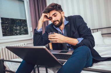 Otel odasında çalışma. Takım elbise ve kravat yatakta otel odasında otururken dizüstü bilgisayar üzerinde çalışan kendine güvenen genç işadamı 