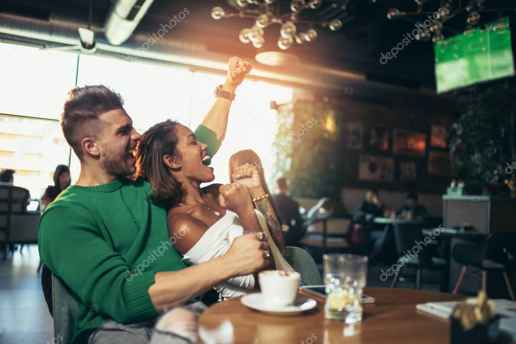 Happy excited couple watching football sitting at cafe