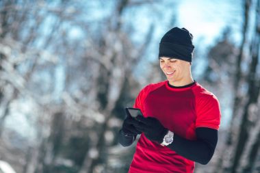 Sportif giysiler kış Park smartphone kullanarak genç adam