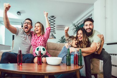 Mutlu arkadaşlar ya da futbol taraftarları televizyonda maç izleyip zaferi evde kutluyorlar. Dostluk, spor ve eğlence kavramı..