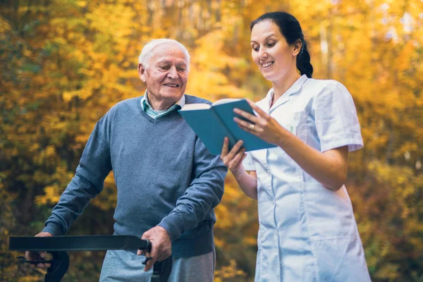 Leende Sjuksköterska Läsa Bok Till Senior Mannen Som Använder Walker — Stockfoto