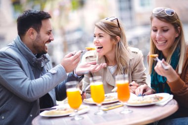 Telefonunuzun açık kafede güneşli günde, pizza yemek üç arkadaş grubu