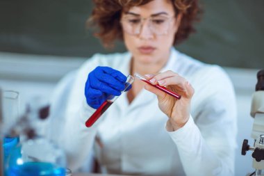 Kadın laboratuarında masada oturan ve kan test tüpü tutan