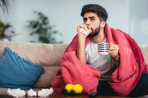 Young ill man drinking hot tea at home and watching tv