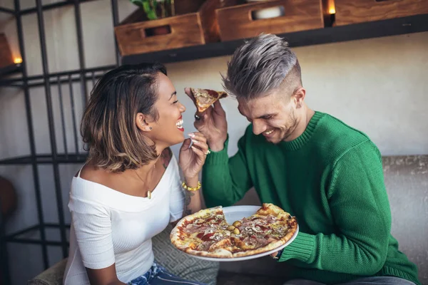 Mixed-race couple eating pizza in modern cafe